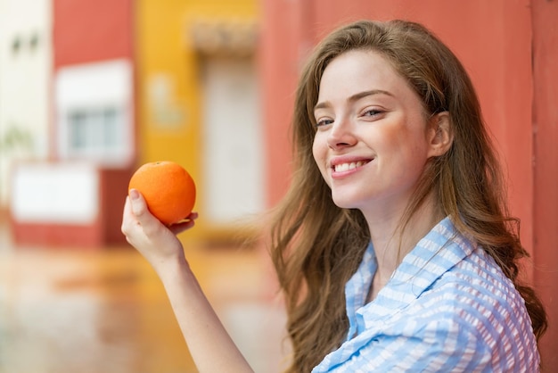 Mulher jovem ruiva ao ar livre segurando uma laranja