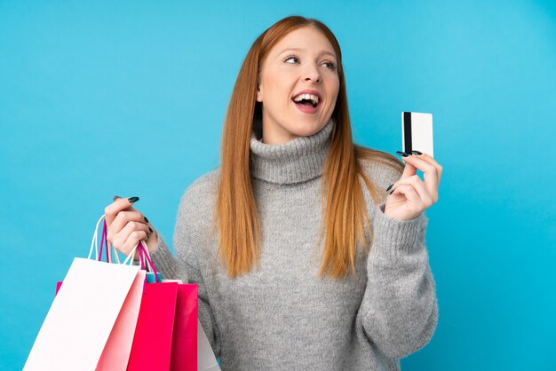 Mulher jovem ruiva azul segurando sacolas de compras e cartão de crédito