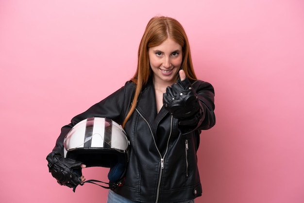 Mulher jovem ruiva com um capacete de moto isolado no fundo rosa, fazendo o próximo gesto