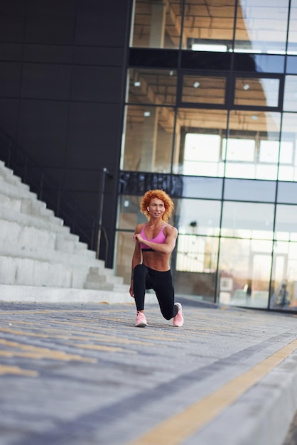 Mulher jovem ruiva europeia em roupas esportivas fazendo agachamentos ao ar livre