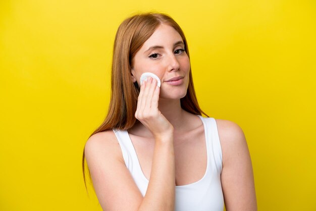 Mulher jovem ruiva isolada em fundo amarelo com almofada de algodão para remover maquiagem do rosto