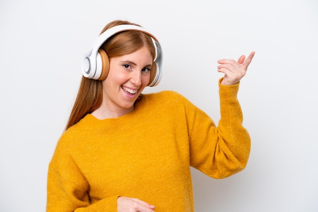 Mulher jovem ruiva isolada em fundo branco ouvindo música e fazendo gesto de guitarra