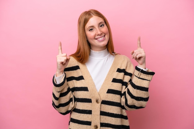 Mulher jovem ruiva isolada em fundo rosa apontando uma ótima ideia