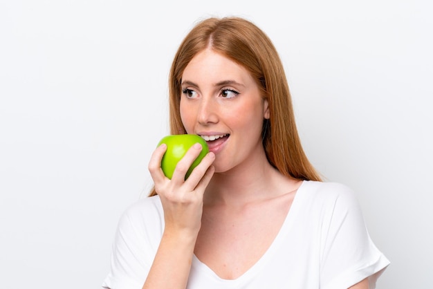 Mulher jovem ruiva isolada no fundo branco comendo uma maçã