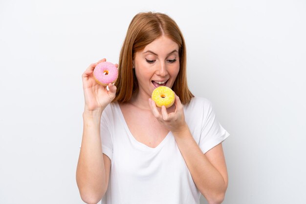 Mulher jovem ruiva isolada no fundo branco comendo uma rosquinha