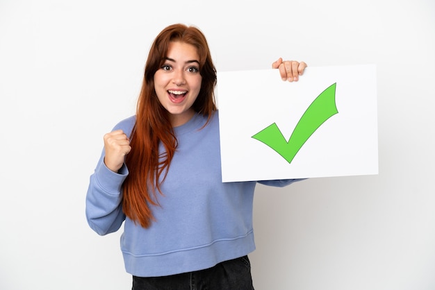 Foto mulher jovem ruiva isolada no fundo branco segurando um cartaz com o texto ícone de marca de seleção verde e comemorando uma vitória