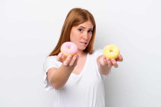 Mulher jovem ruiva isolada no fundo branco segurando uma rosquinha e triste