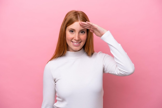 Mulher jovem ruiva isolada no fundo rosa saudando com a mão com expressão feliz