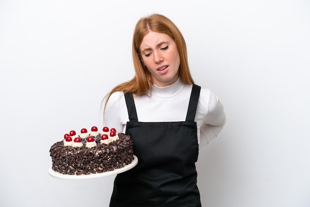 Mulher jovem ruiva segurando bolo de aniversário isolado no fundo branco, sofrendo de dor nas costas por ter feito um esforço