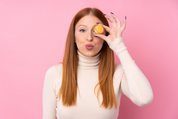 Mulher jovem ruiva segurando macarons franceses coloridos com cara engraçada