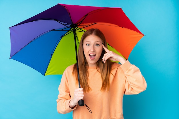 Mulher jovem ruiva segurando um guarda-chuva sobre parede isolada, pretendendo realizar a solução