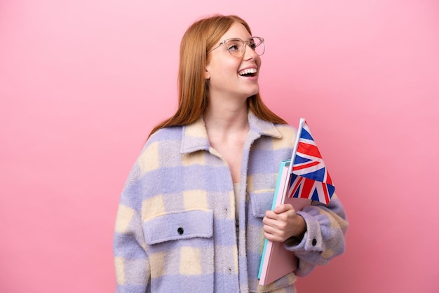 Mulher jovem ruiva segurando uma bandeira do Reino Unido isolada em fundo rosa rindo