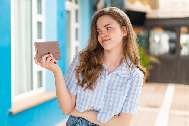 Mulher jovem ruiva segurando uma carteira ao ar livre com expressão triste