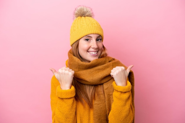 Mulher jovem ruiva vestindo jaqueta de inverno isolada em fundo rosa com polegares para cima gesto e sorrindo