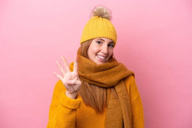 Mulher jovem ruiva vestindo jaqueta de inverno isolada em fundo rosa feliz e contando quatro com os dedos