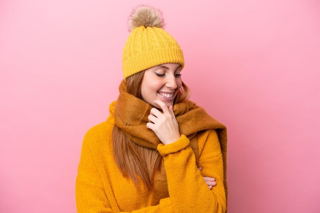 Mulher jovem ruiva vestindo jaqueta de inverno isolada em fundo rosa, olhando para o lado