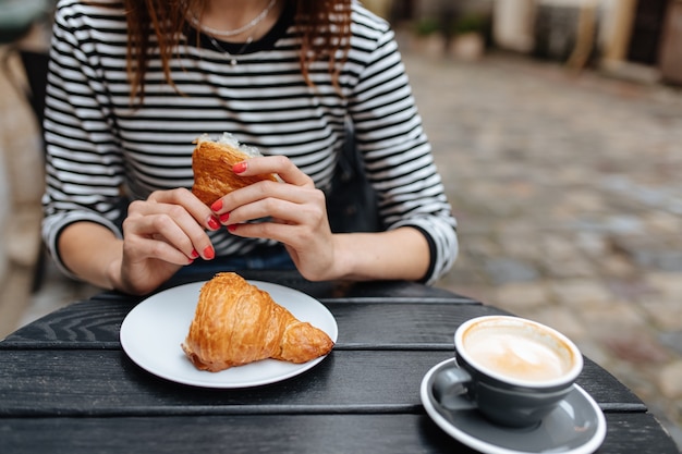 Foto mulher jovem saboreando um croissant recém-assado e um café saboroso no terraço do café