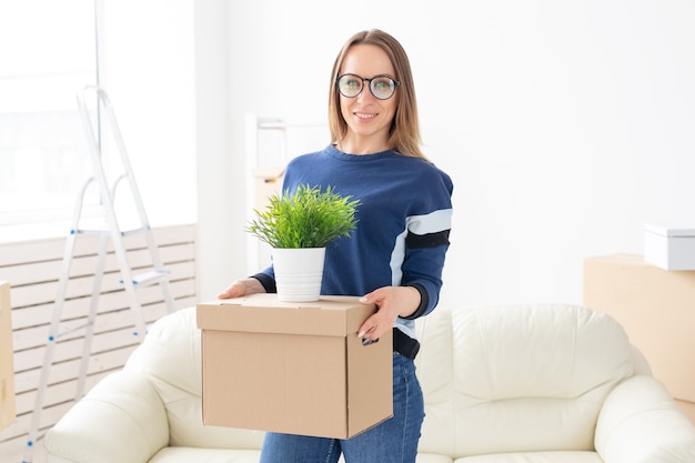 Mulher jovem segura uma caixa e um vaso de plantas enquanto se muda para um novo apartamento. festa de inauguração e novo conceito de habitação.