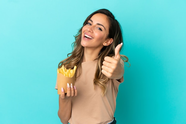 Mulher jovem segurando batatas fritas sobre um fundo isolado com o polegar para cima porque algo bom aconteceu