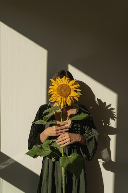Mulher jovem segurando caule de girassol amarelo sombras estéticas de luz solar conceito de moda de beleza floral