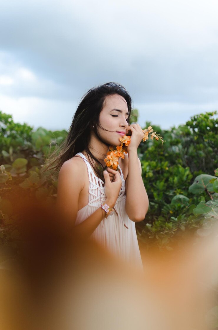 Foto mulher jovem segurando flores de laranja contra árvores contra o céu