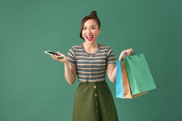 Mulher jovem segurando sacolas de compras e um telefone celular