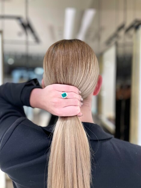 Mulher jovem segurando seu cabelo loiro com uma mão usando anel de esmeralda e diamante foto de alta qualidade