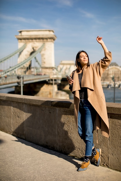 Mulher jovem, segurando, telefone móvel, com, ponte chain, em, fundo, em, budapest