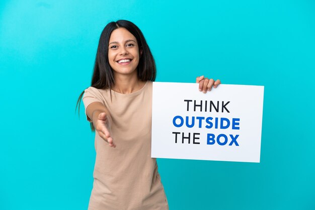 Mulher jovem segurando um cartaz com o texto Pense fora da caixa fazendo um acordo sobre um fundo isolado