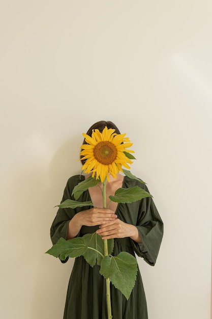 Mulher jovem segurando um caule amarelo de girassol em fundo branco Conceito de moda de beleza floral estética