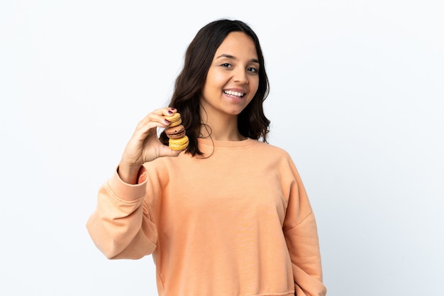 Mulher jovem segurando um fundo branco isolado, segurando macarons franceses coloridos e com uma expressão feliz