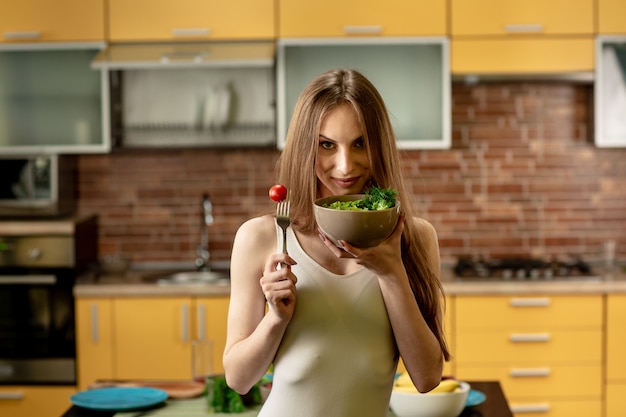 Mulher jovem segurando um garfo com tomate cereja e uma tigela de salada