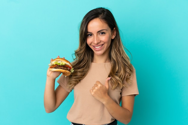 Mulher jovem segurando um hambúrguer sobre um fundo isolado e fazendo um gesto de polegar para cima