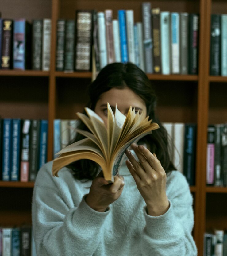 Foto mulher jovem segurando um livro contra uma prateleira na biblioteca