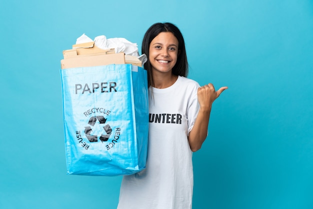 Mulher jovem segurando um saco de reciclagem cheio de papel apontando para o lado para apresentar um produto