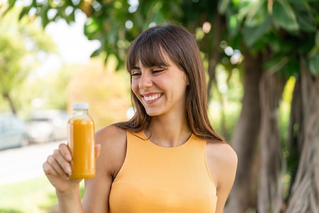 Mulher jovem segurando um suco de laranja ao ar livre com expressão feliz