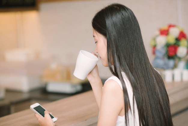 Mulher jovem, segurando, um, xícara café, e, usando, dela, telefone móvel