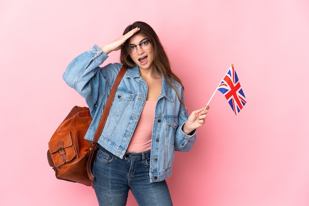 Mulher jovem segurando uma bandeira do Reino Unido isolada em rosa com expressão de surpresa