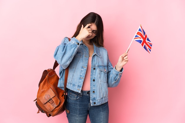 Mulher jovem segurando uma bandeira do Reino Unido isolada na parede rosa rindo