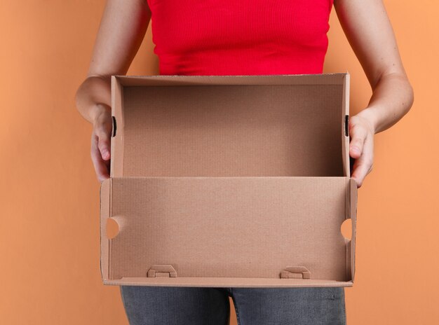 Mulher jovem segurando uma caixa de papelão vazia em laranja