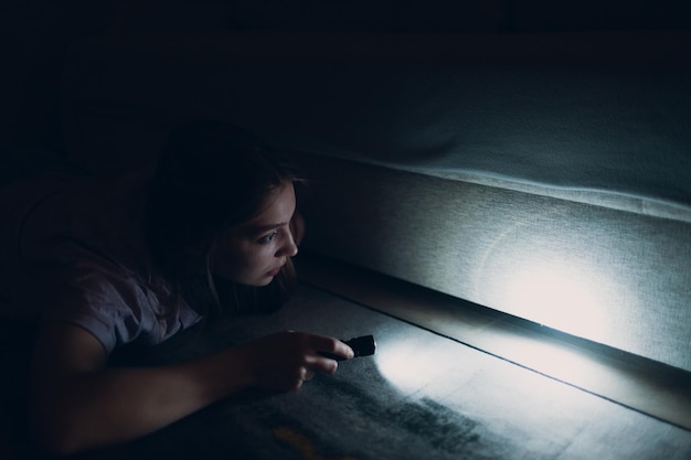 Mulher jovem segurando uma lanterna de mão procurando por sujeira sob móveis