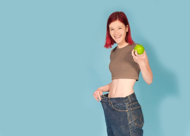 Mulher jovem segurando uma maçã verde e usando calças grandes