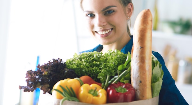 Mulher jovem segurando uma sacola de compras de supermercado com legumes em pé na cozinha