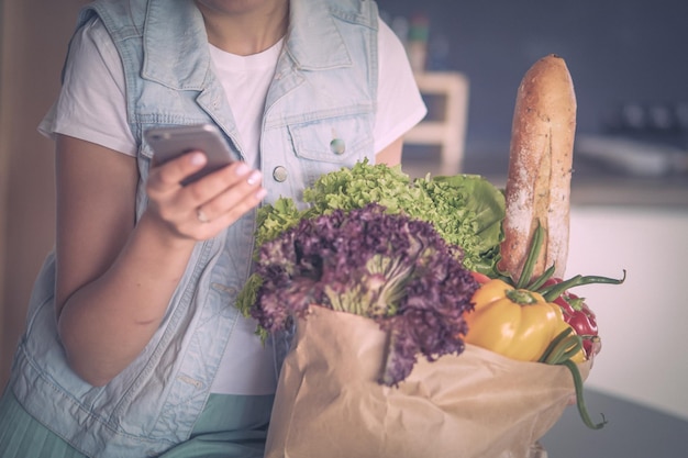 Mulher jovem segurando uma sacola de compras de supermercado com legumes em pé na cozinha