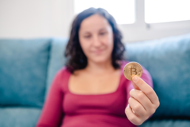 Mulher jovem sem foco com uma moeda bitcoin na mão em casa