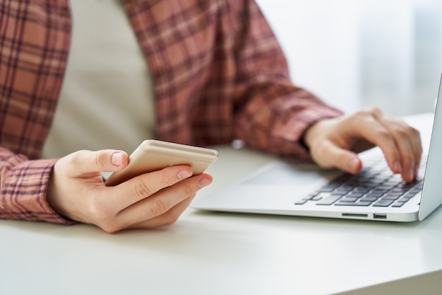 Mulher jovem sem rosto navegando em smartphone enquanto digita no laptop conceito de privacidade de dados milenar