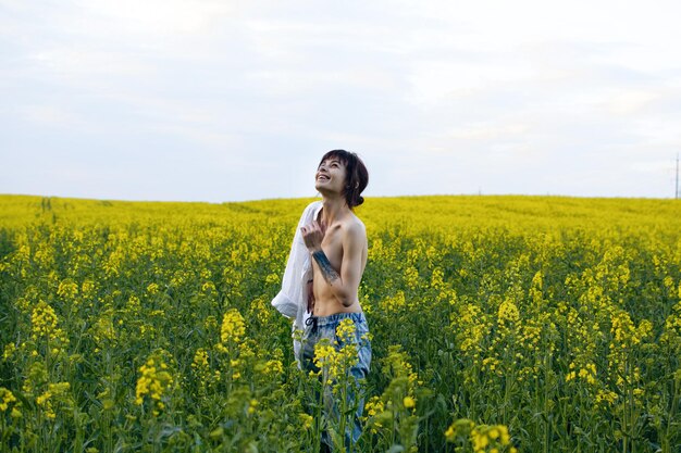 Mulher jovem sensual com tatuagens posando em um campo de colza entre flores amarelas em um dia ensolarado.