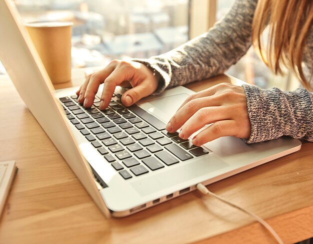 Mulher jovem sentada à mesa trabalhando com seu laptop moderno