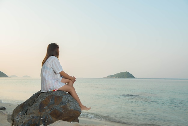 Mulher jovem sentada em uma rocha, apreciando a praia e o mar