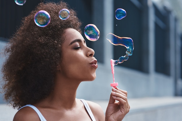 Foto mulher jovem sentada na rua soprando bolhas de alegria no estilo livre